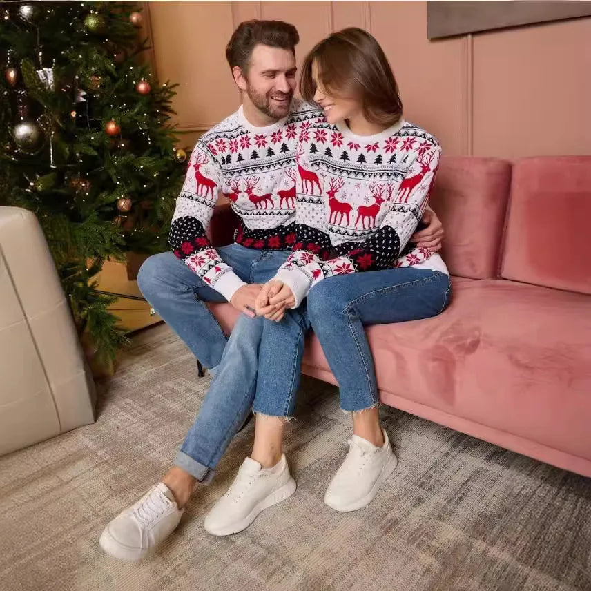 Par i vita jultröjor sittande i en rosa soffa vid julgranen